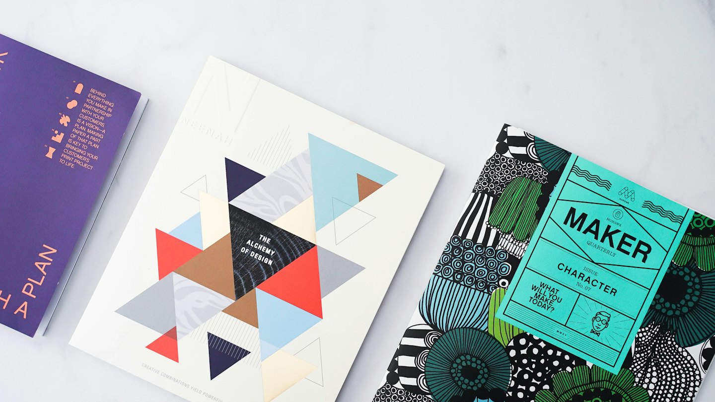 Three design magazines lie open on a white desk.